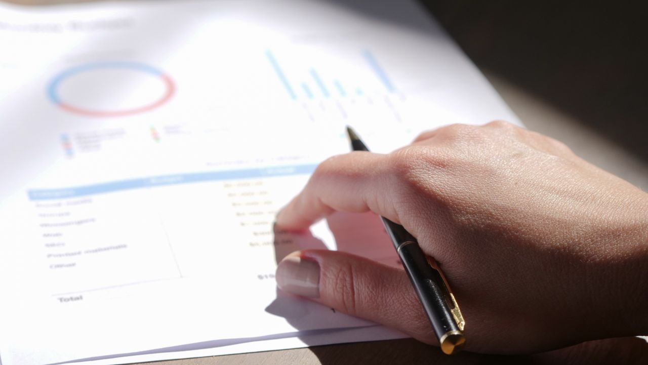digital A close-up view of a hand holding a pen and examining financial charts on paper.